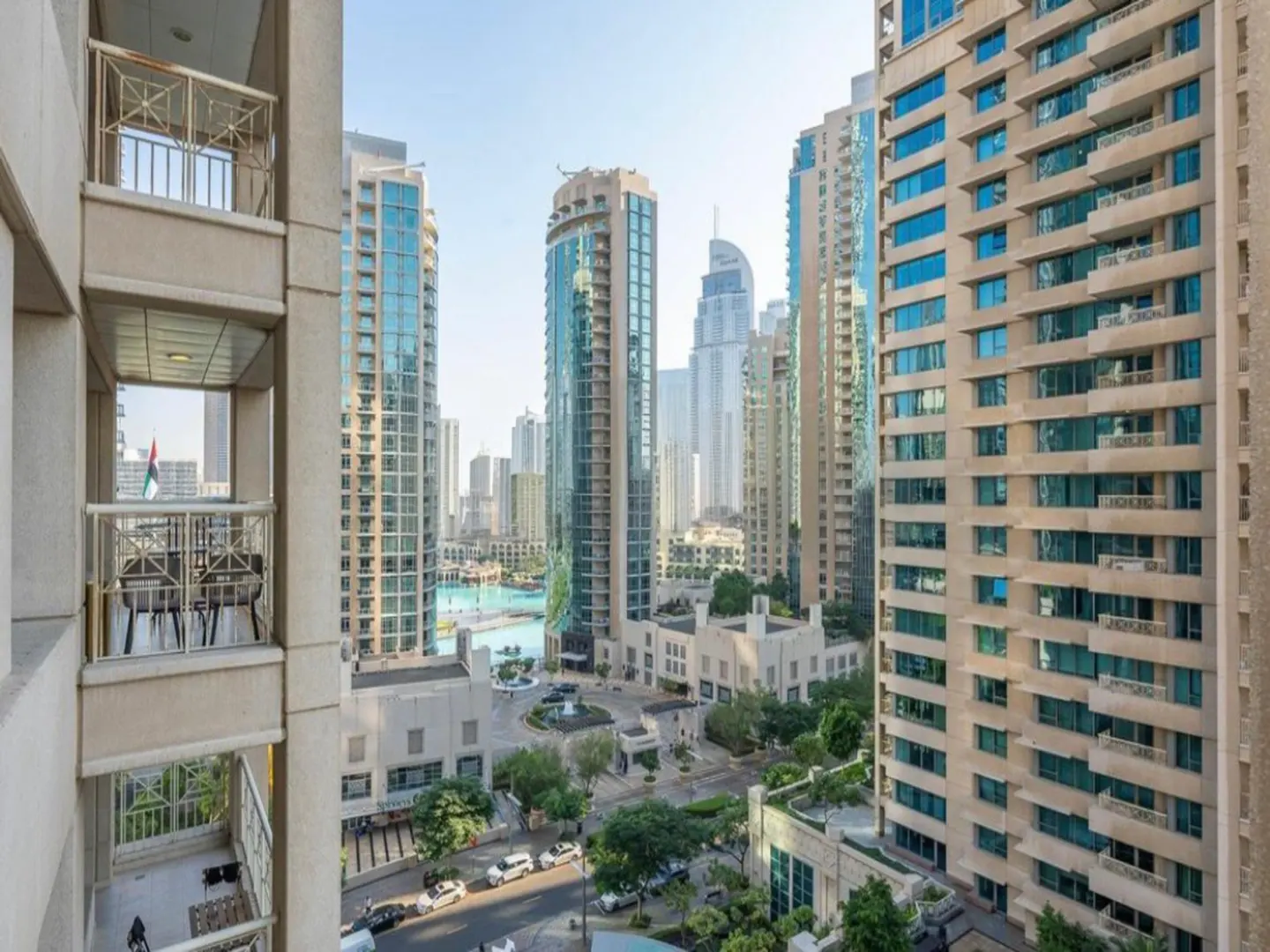 View from a high-rise balcony overlooking a cityscape with tall buildings, a water feature, and street traffic below.