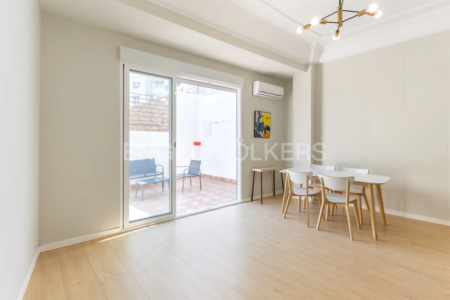 Bright dining room with light wood floors, white walls, and a modern chandelier. Sliding glass doors open to a patio with outdoor seating.