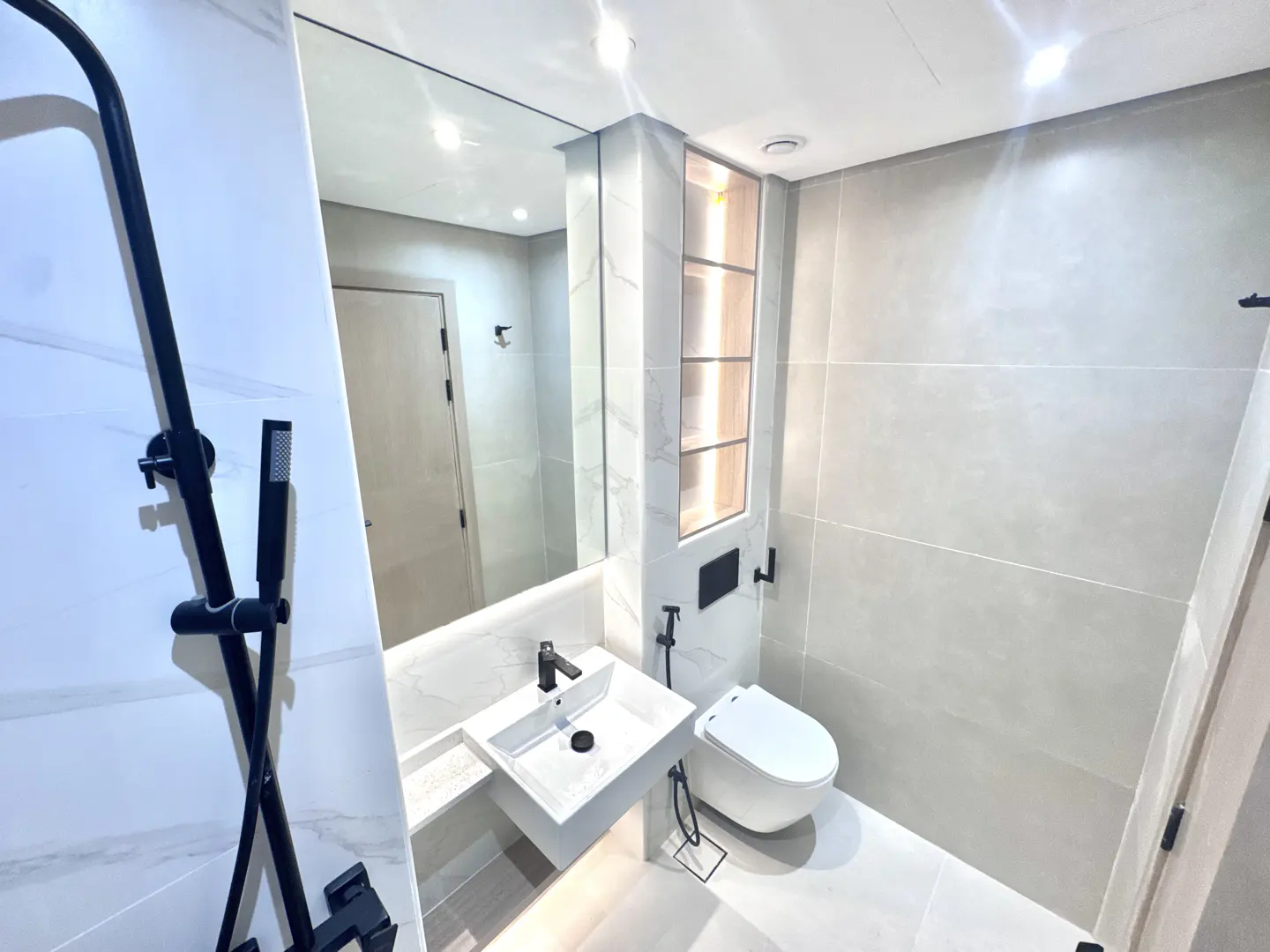 Modern bathroom with white tiles, a square sink with black faucet, and a black shower fixture. A mirror reflects the room.