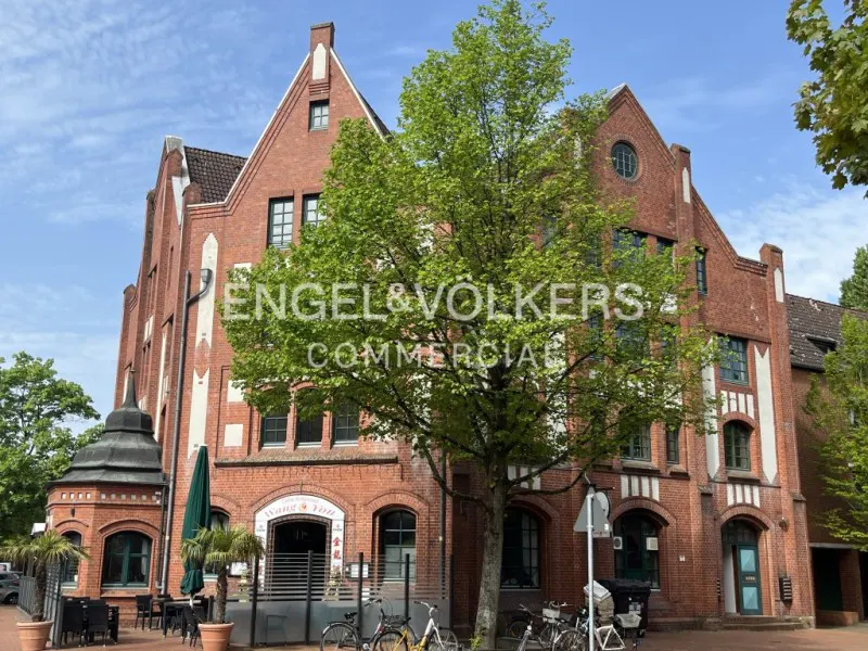 Exterior of a red brick commercial building with a restaurant, bikes parked in front. Engel & Völkers logo is visible.