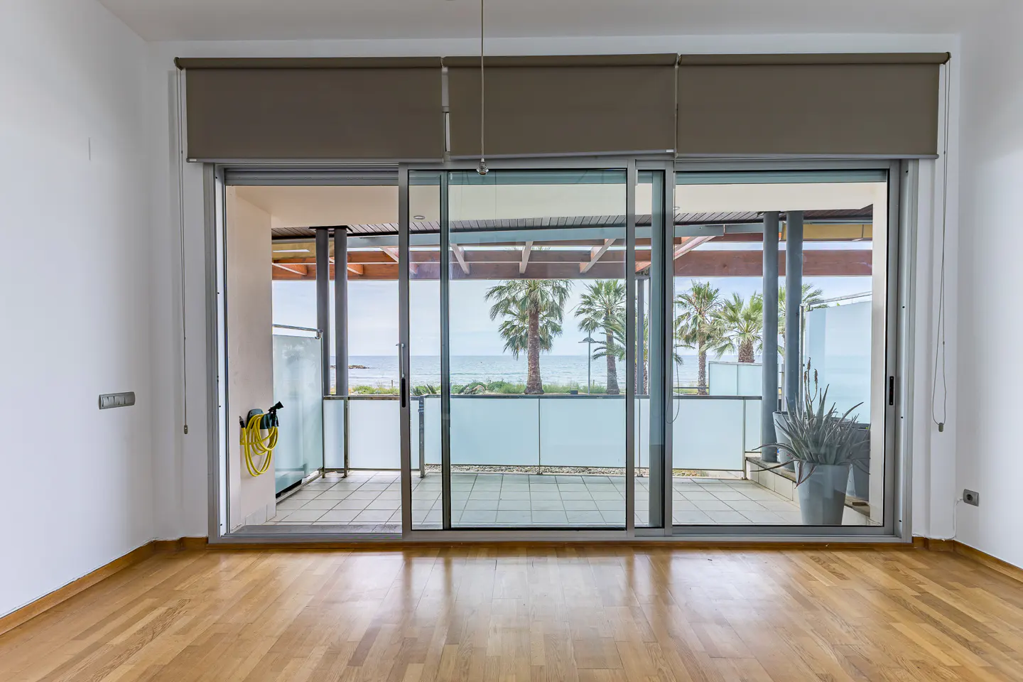 Empty room with hardwood floors and large sliding glass doors opening to a balcony with palm trees and ocean views.
