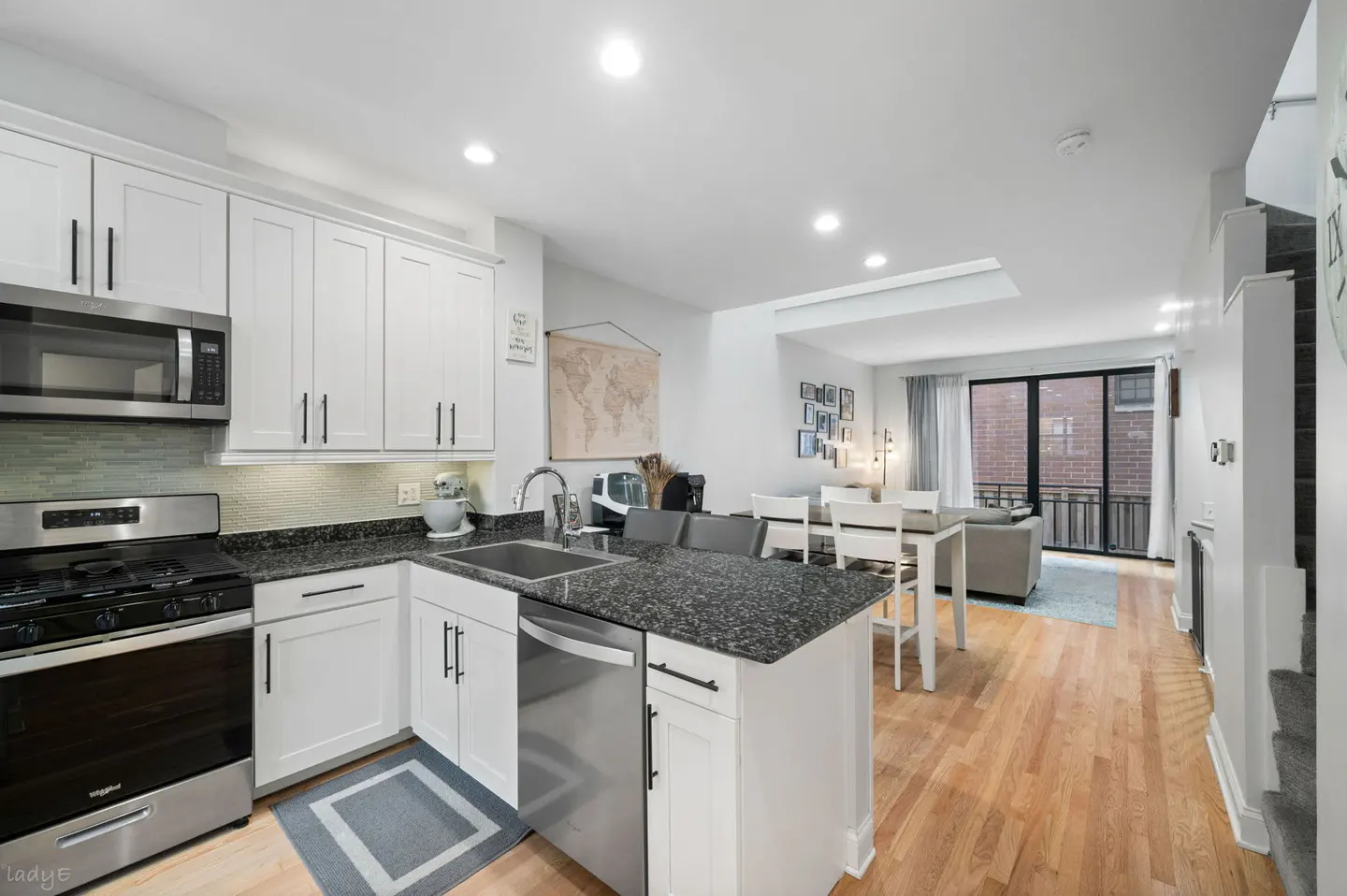 Bright, modern kitchen with white cabinets, black granite countertops, and stainless steel appliances. Open floor plan leads to a dining area and living room.