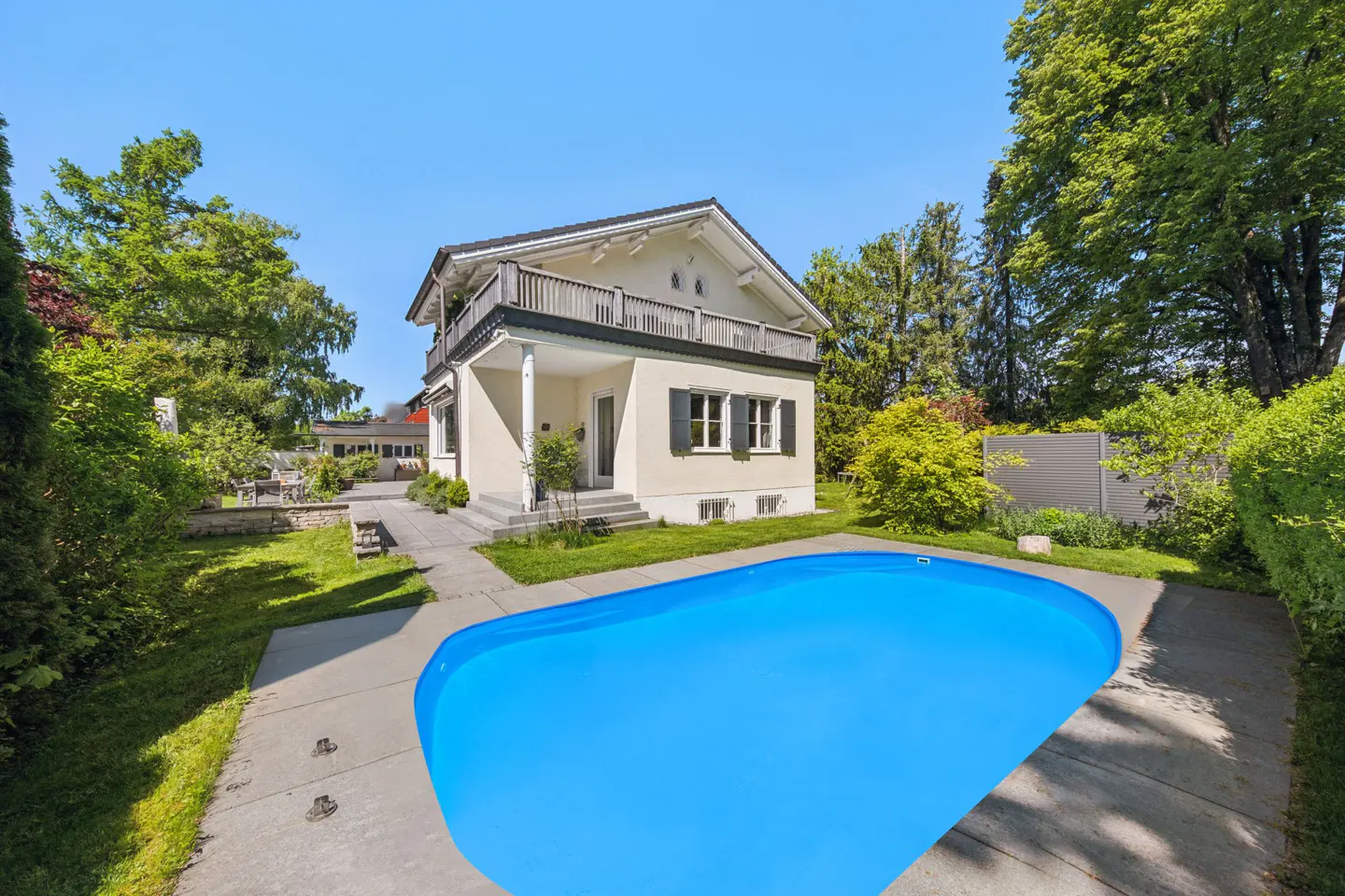 Two-story house with a balcony, black shutters, and a bright blue pool in the backyard.