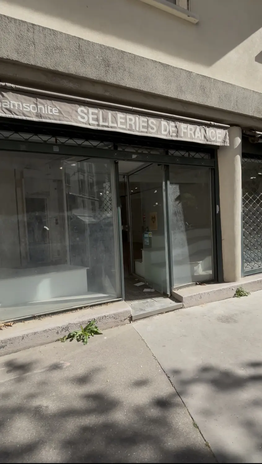 Exterior of "Selleries de France" store with glass windows and metal security shutters, partially open.