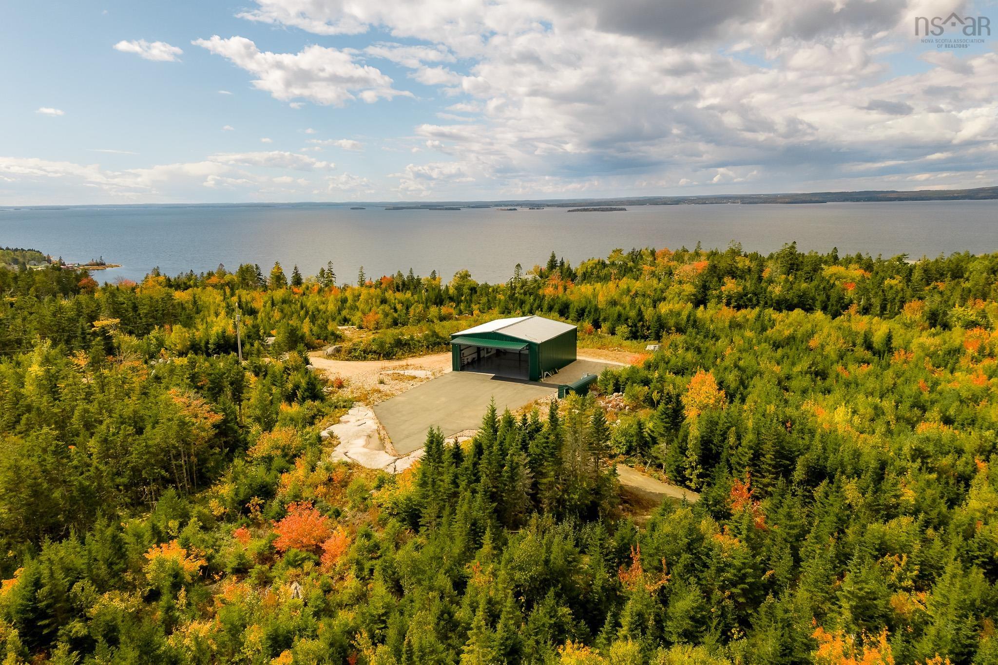 Aerial view of a green metal garage set in a dense forest with autumn colors, overlooking a large body of water. [AI-generated text]