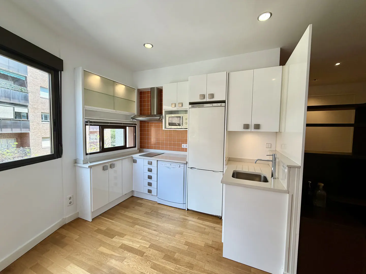 Bright kitchen with white cabinets, stainless steel appliances, and wood floors. A window overlooks a building.