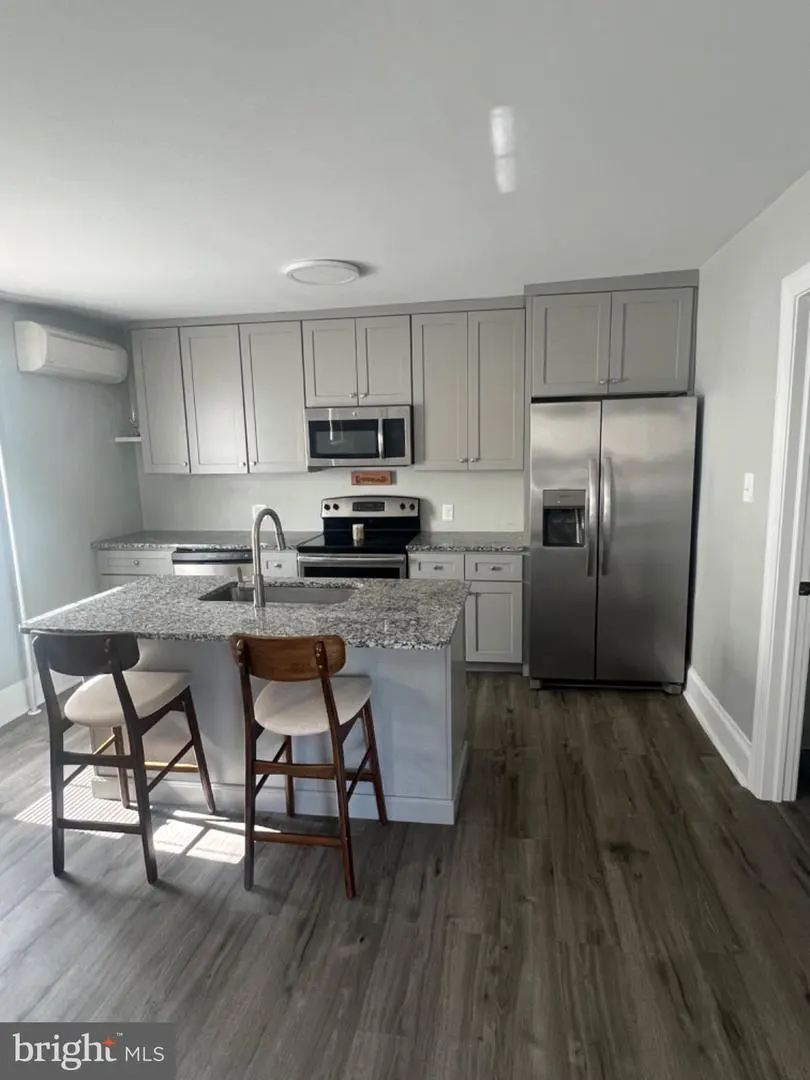 A kitchen with gray cabinets, stainless steel appliances, granite countertops, and a center island with two chairs.