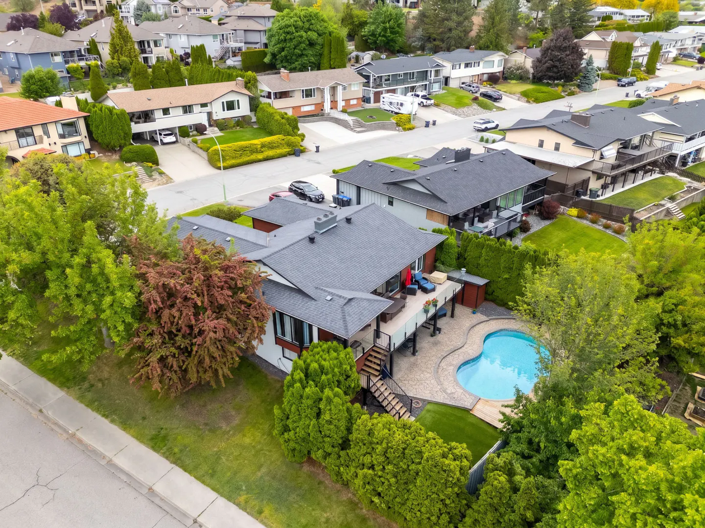 Aerial view of a white house with a gray roof, a pool, and a deck in a suburban neighborhood.