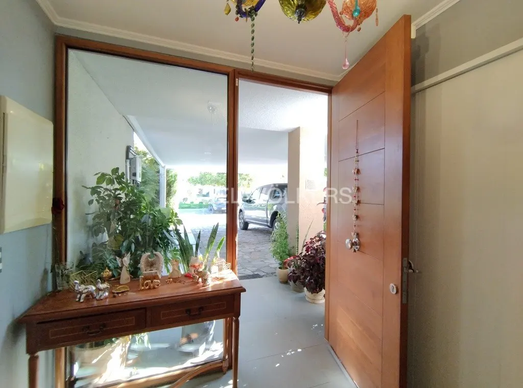 Open wooden front door with decorative hanging, table with plants, and view of driveway with car.