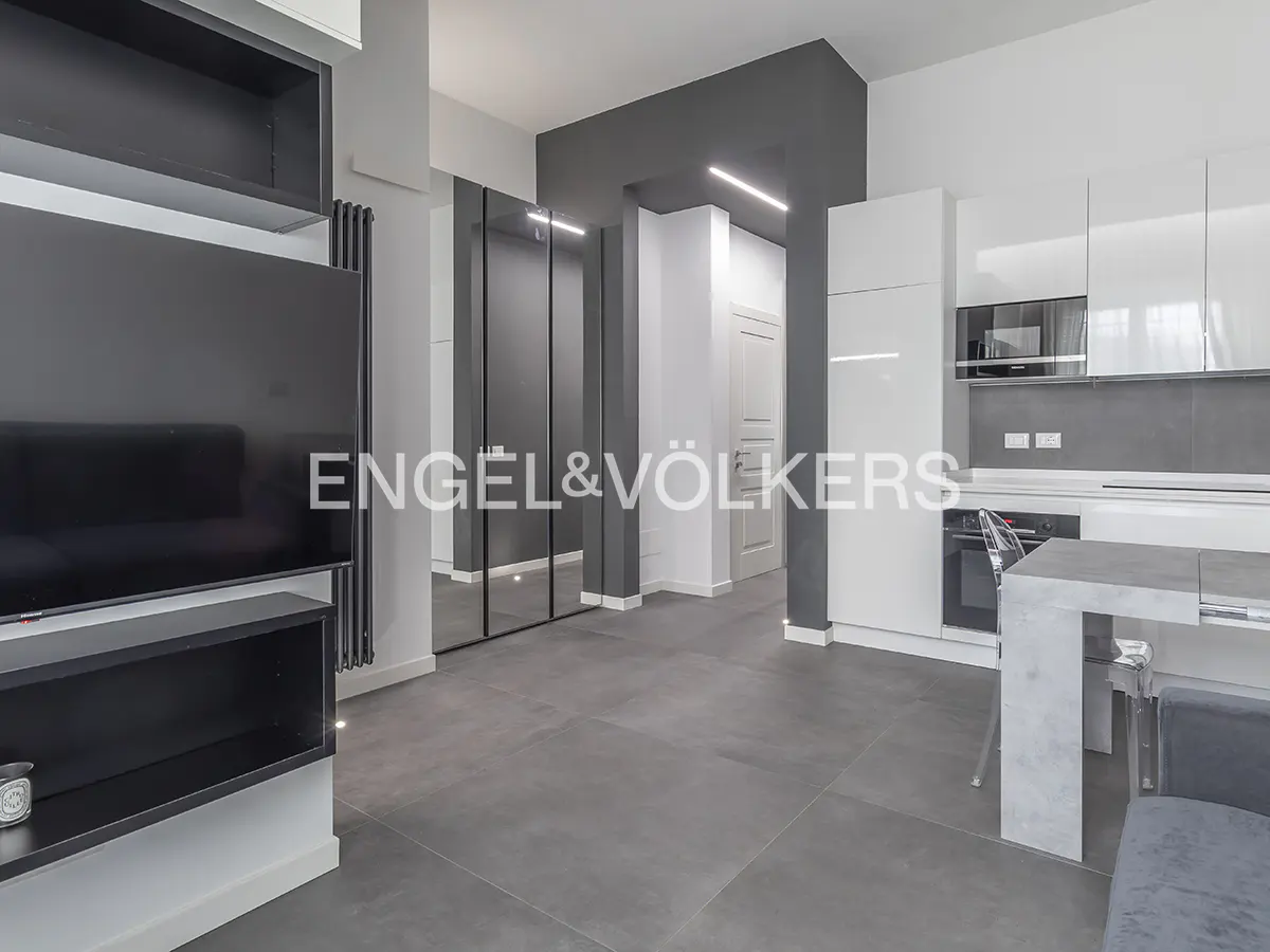 Modern open-plan apartment with a black media unit, grey tiled floors, and a sleek white kitchen with a dining table.
