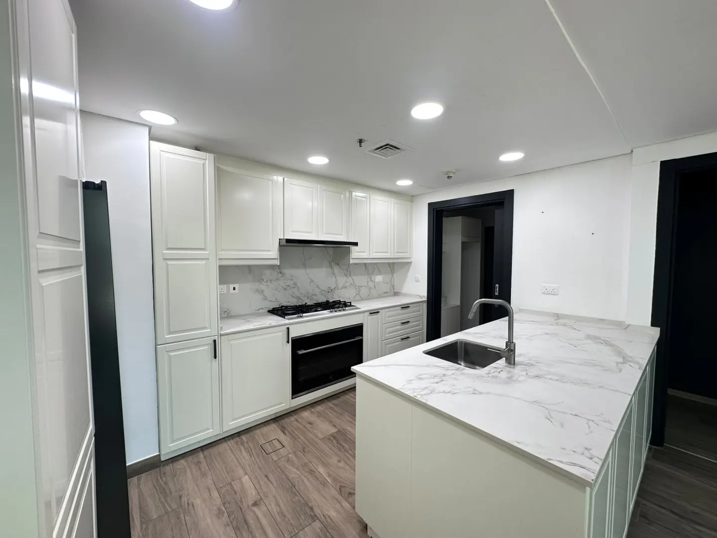 Modern kitchen with white cabinets, marble countertops, a central island with a sink, and wood-look flooring.