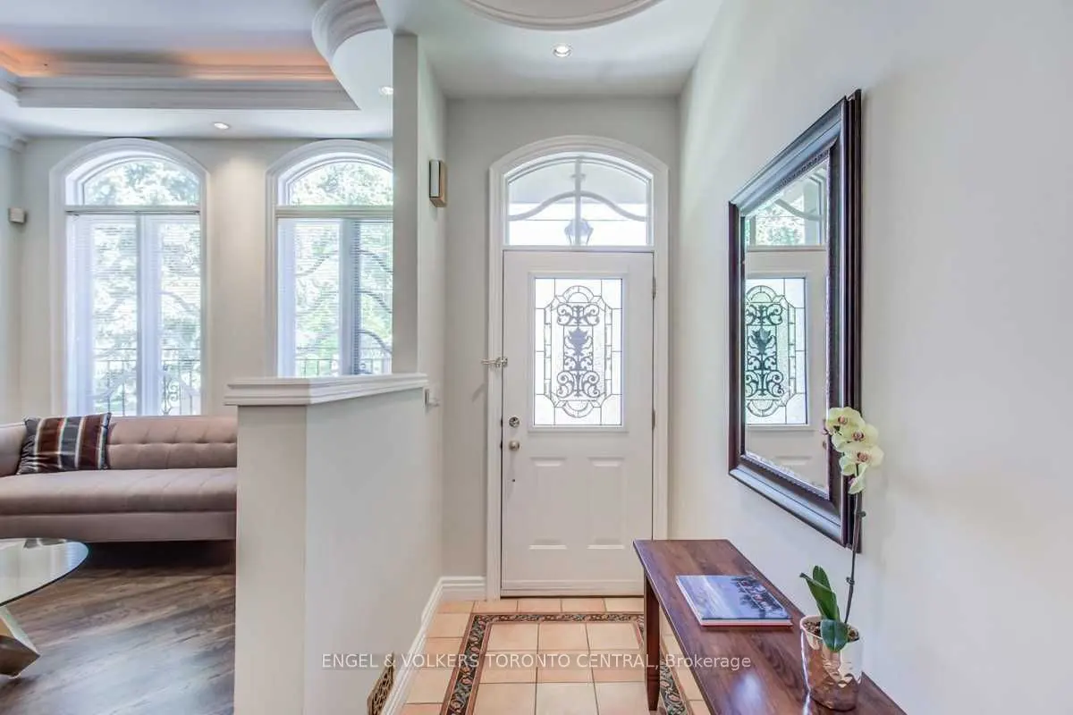 A bright foyer with a white door with decorative glass, a dark wood table, and a framed mirror. An orchid sits on the table.