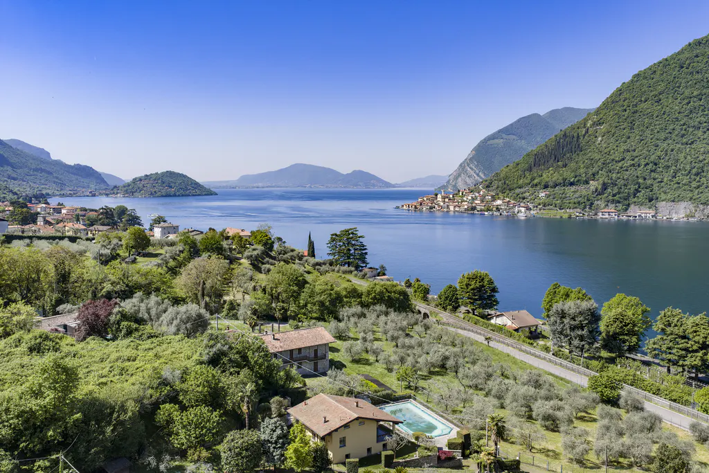 Scenic view of Lake Iseo, Italy, with mountains, blue water, and lush green landscape. Houses with pools dot the hillside.
