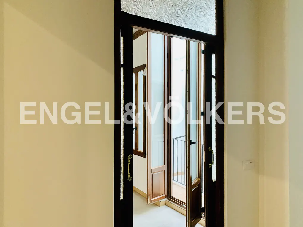 Dark wooden doorway with glass panels opening to a bright balcony with a metal railing.