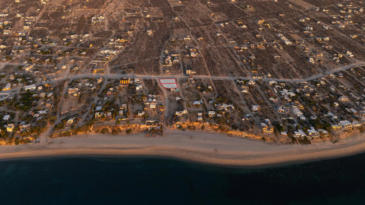 Aerial view of a coastal town with a sandy beach and blue ocean. Two adjacent lots are outlined in red.