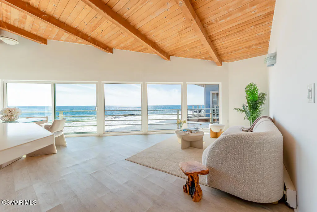 Bright living room with ocean view. White walls, wood ceiling, large windows, and modern furniture.