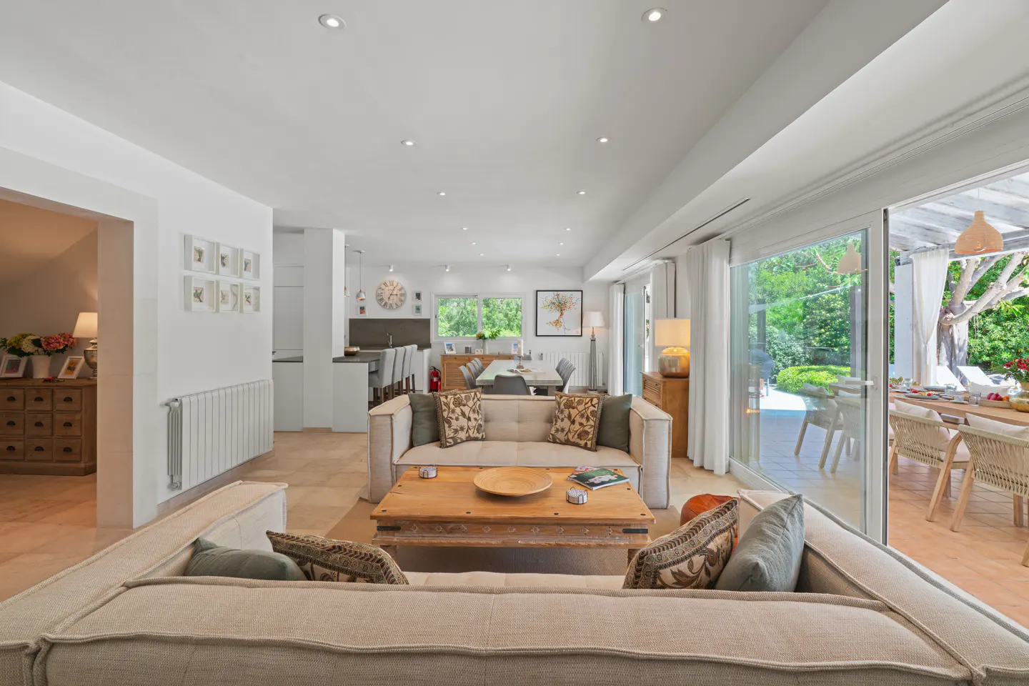 Bright, open living room with beige sofas, wooden coffee table, and sliding glass doors to an outdoor dining area.