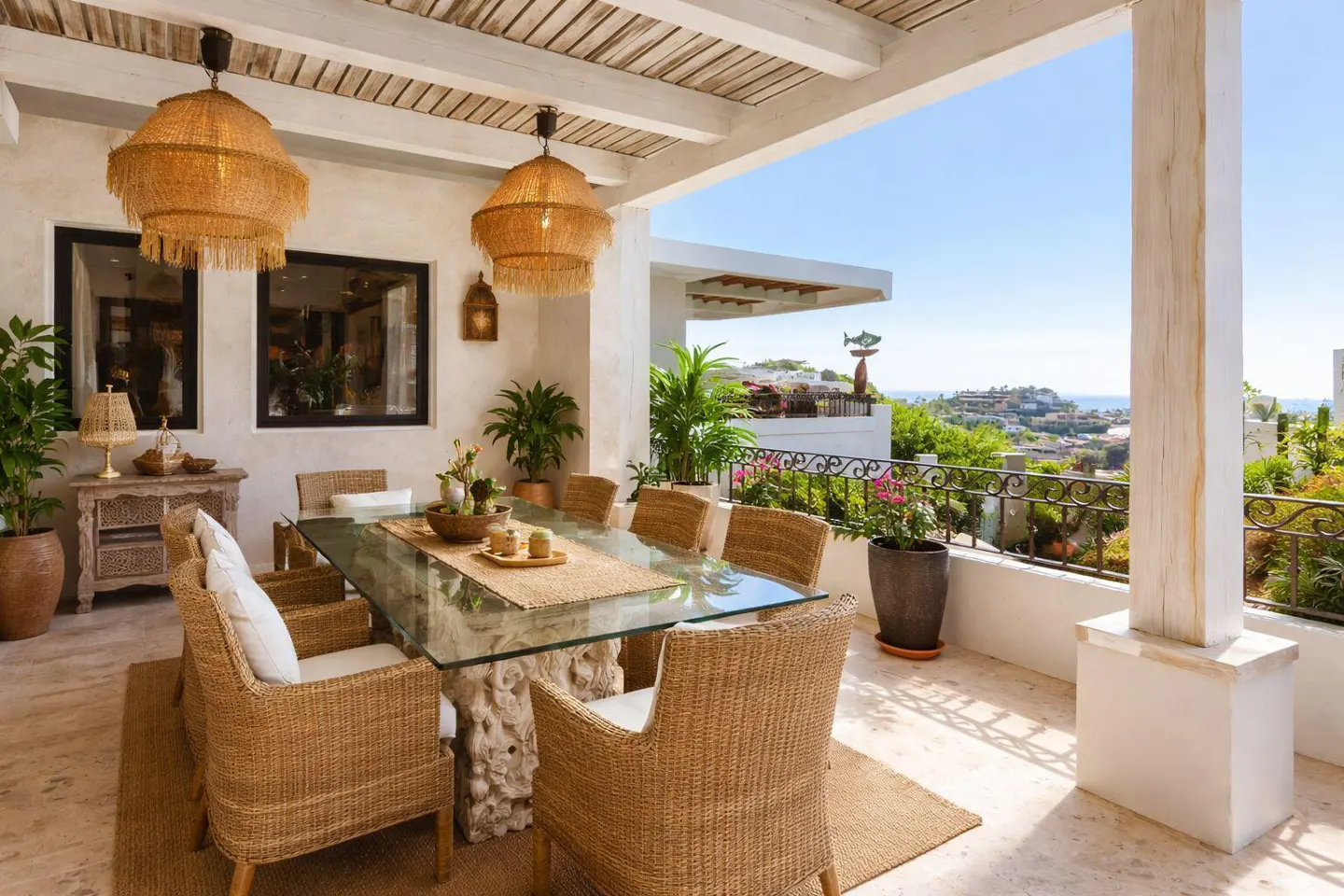 Outdoor dining area with wicker chairs, glass table, and straw pendant lights. Ocean view in the background.