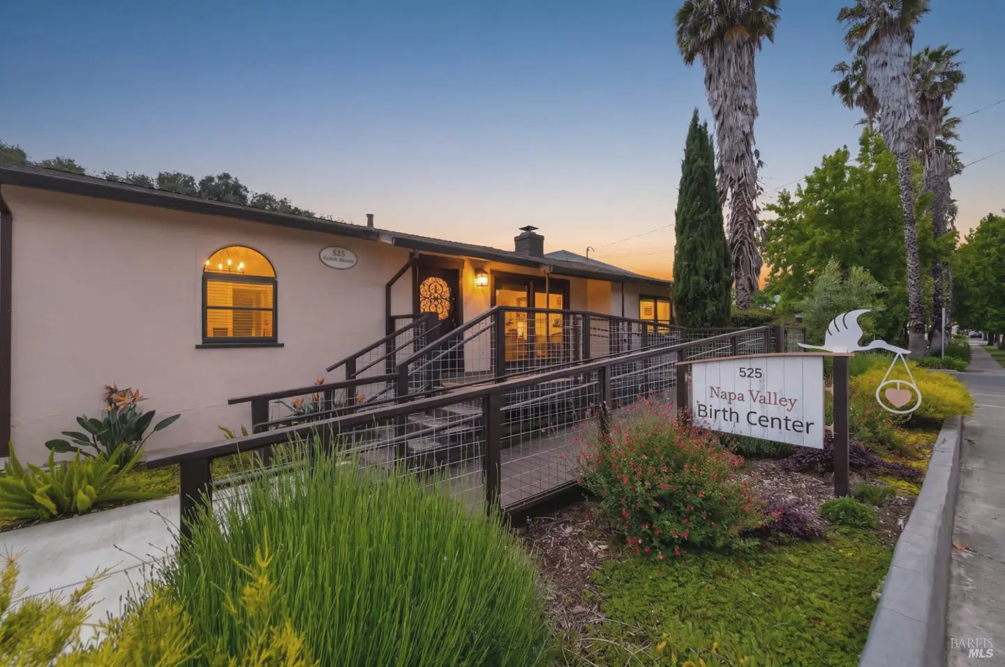 Exterior view of Napa Valley Birth Center with a sign featuring a stork carrying a baby. The building is beige with dark trim.