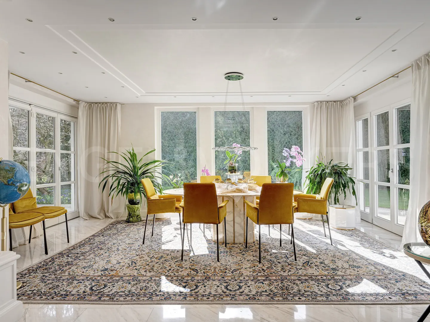 Bright dining room with a marble table, mustard yellow velvet chairs, and a large patterned rug on a white marble floor.