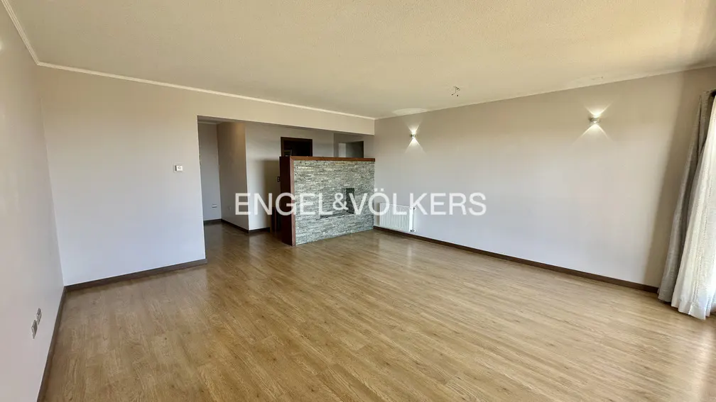 Spacious living room with light wood floors, beige walls, and a stone fireplace. Engel & Völkers logo overlayed on the image.