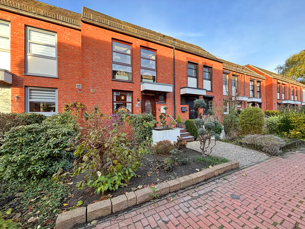 Row of red brick townhouses with manicured front gardens and brick paved walkway.