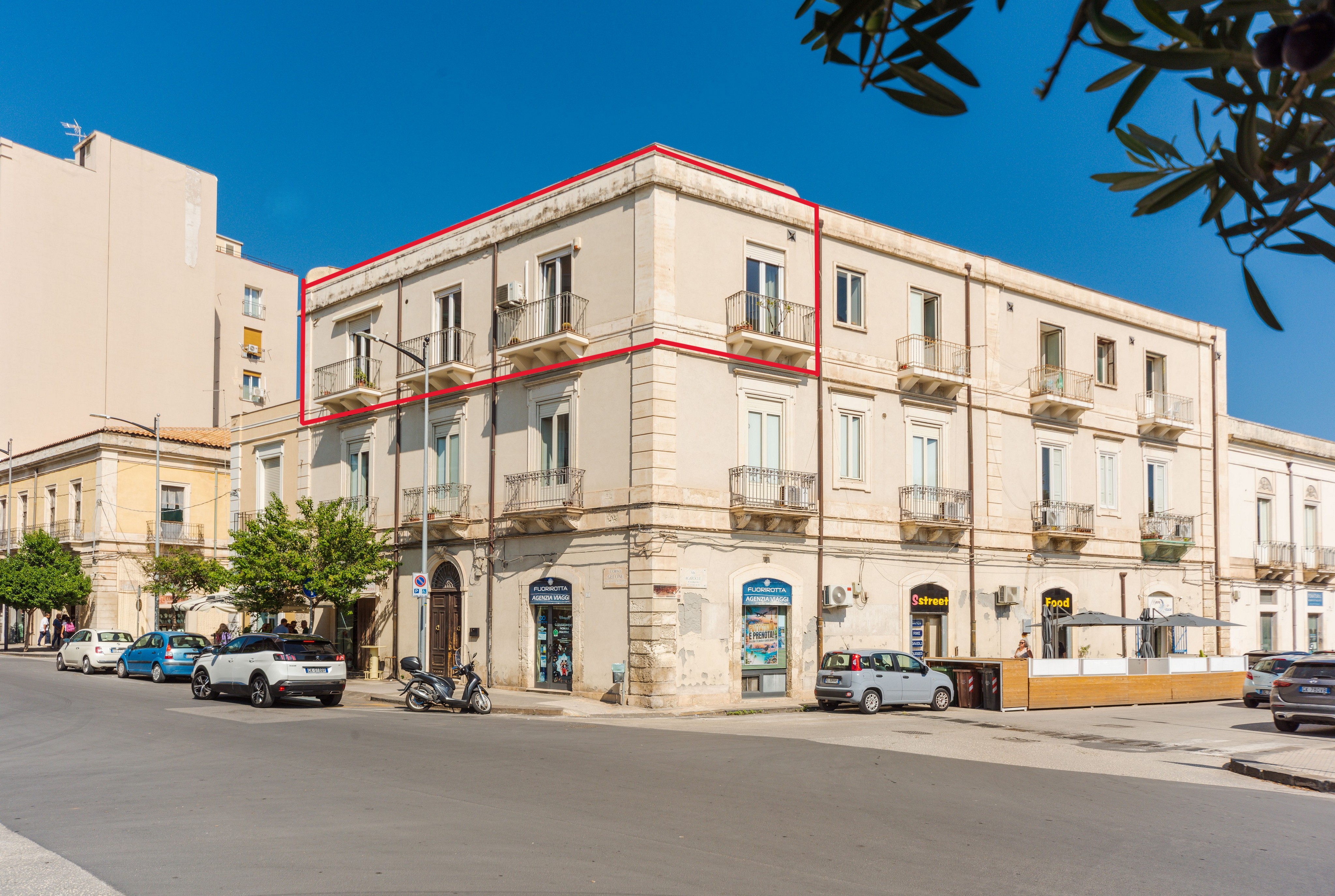 Corner view of a beige multi-story building with a red outline highlighting the top floor apartments under a clear blue sky. [AI-generated text]
