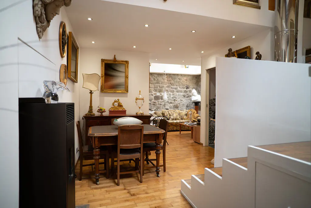 Dining area with wooden table and chairs, adjacent to a living room with a stone wall and hardwood floors.