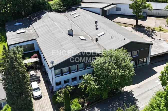 Aerial view of a commercial building with a dark grey roof, white walls, and a white car parked in the driveway.