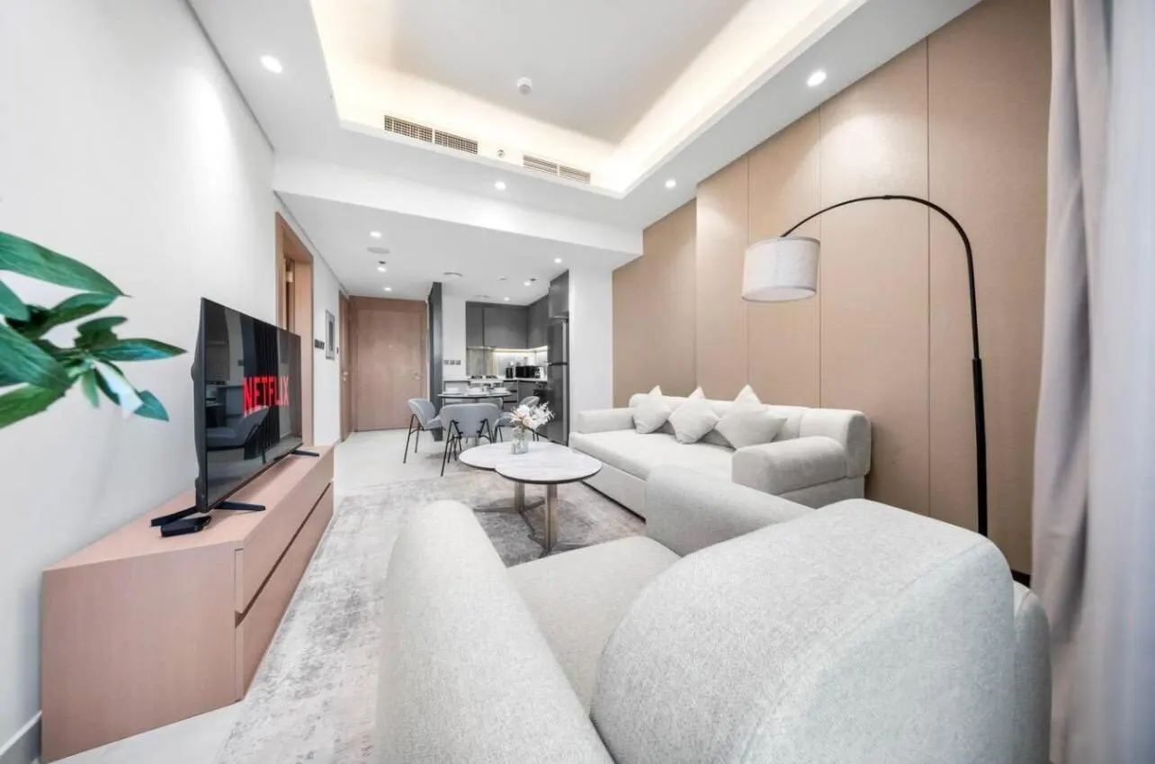 Bright, modern apartment living room with white sofa, TV with Netflix, and open kitchen in the background.