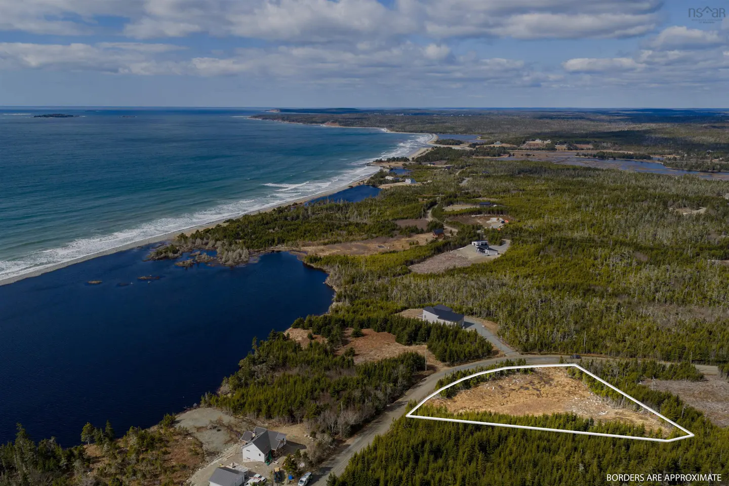 Aerial view of a wooded lot outlined in white, near the ocean and a beach. Houses are visible nearby.