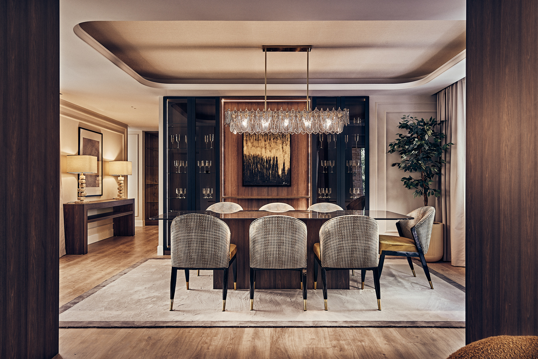 Modern dining room with a glass table, textured chairs, a crystal chandelier, and dark wood cabinetry on a light rug.