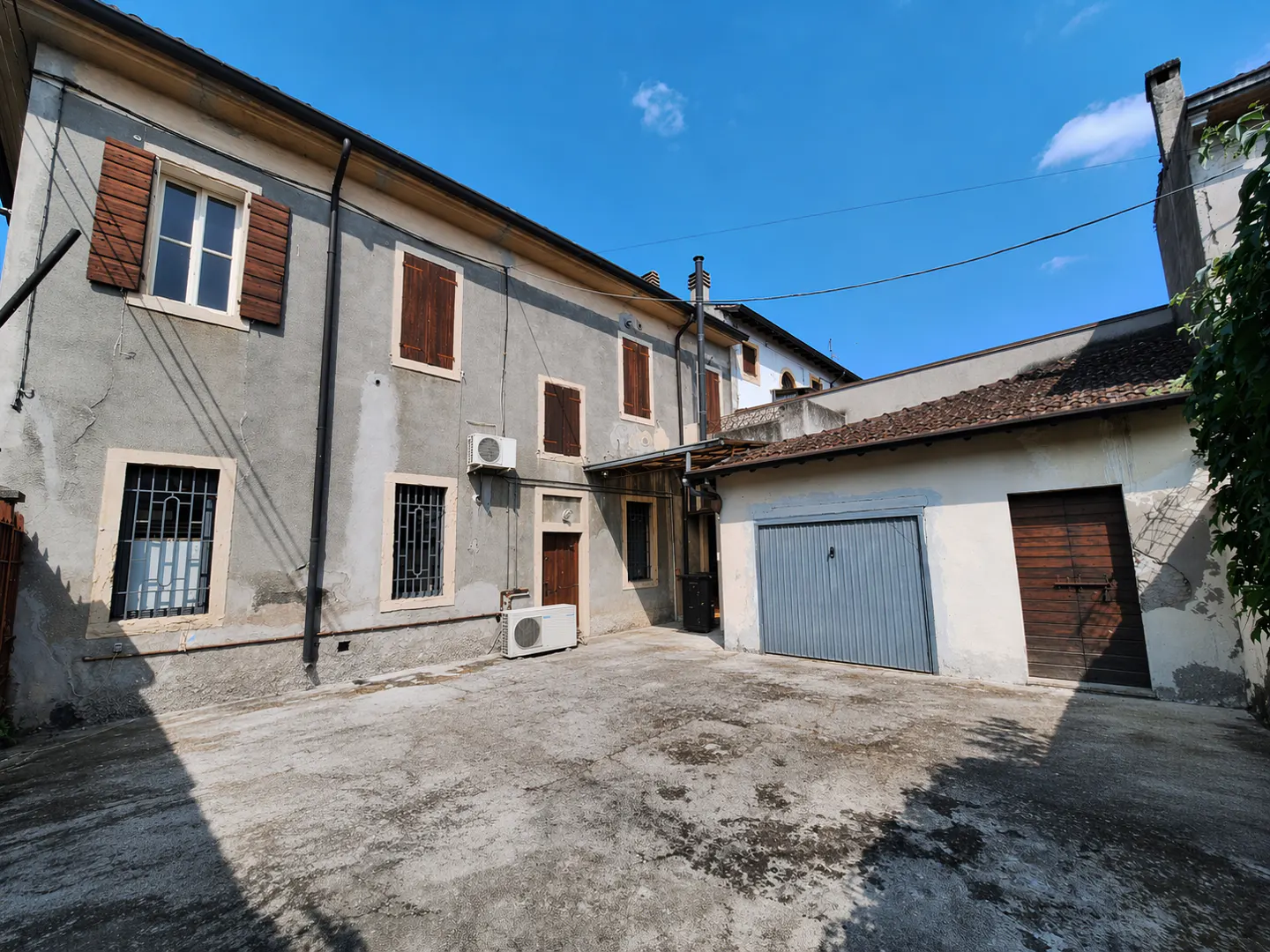 Exterior view of a two-story gray building with brown shutters and a blue garage door under a clear blue sky.