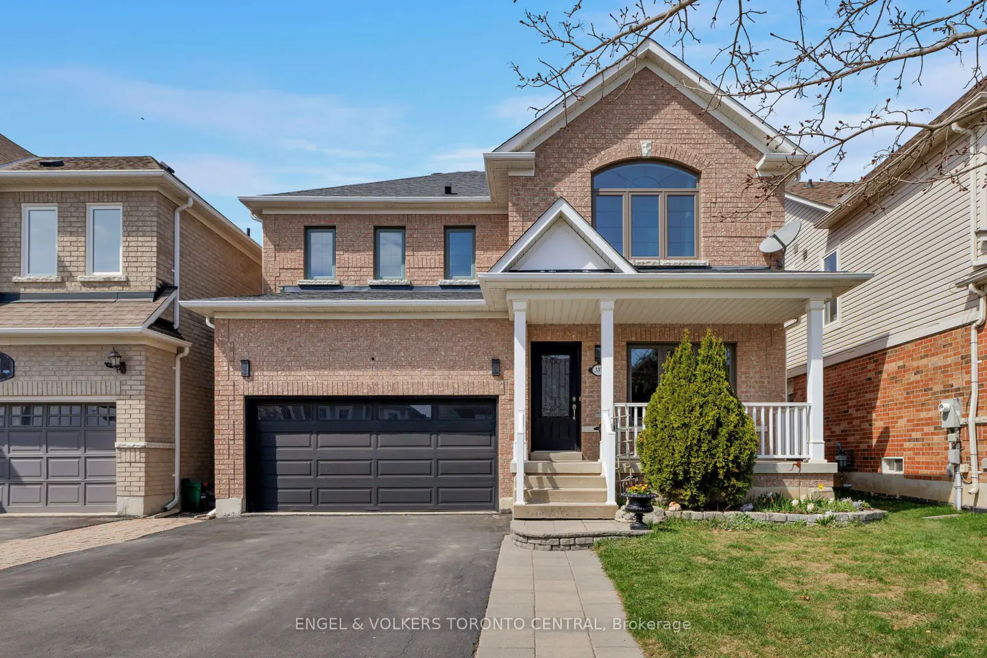 Two-story brick house with a black garage door, front porch with white columns, and green lawn.