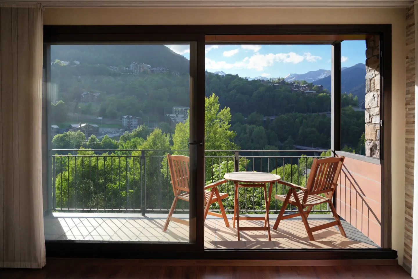 View from a balcony with a table and two chairs overlooking a green valley and mountains.