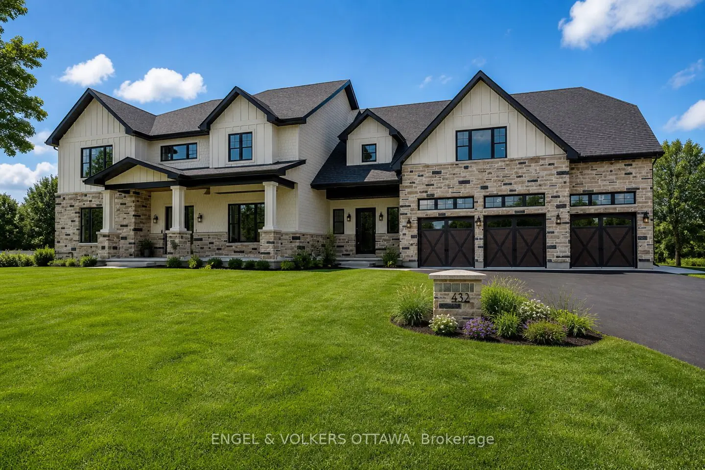 A large, two-story house with a stone and white facade, black trim, and a green lawn. A driveway leads to a three-car garage.