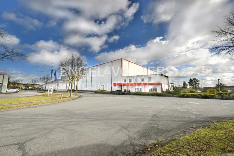 Exterior view of a large, white commercial building with a red trim, under a cloudy sky.