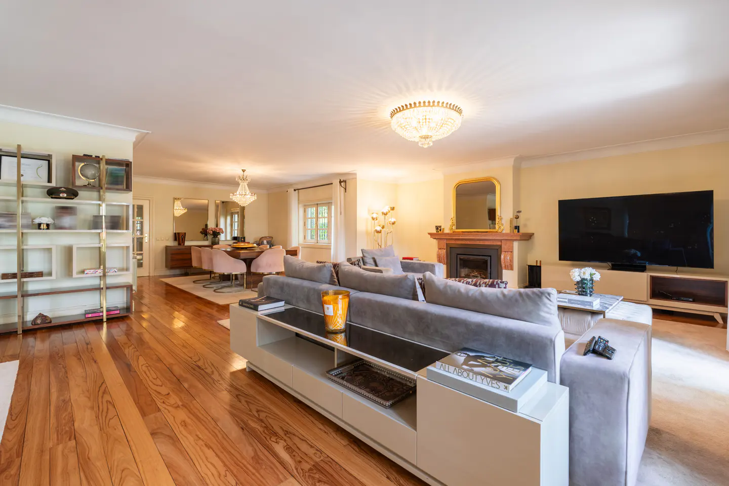 Open-concept living and dining room with hardwood floors, a gray sofa, a fireplace, and a large TV.
