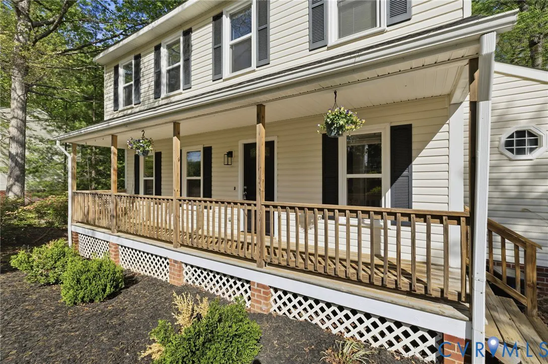 Two-story house with a large porch, wooden railings, and hanging flower baskets. The house is light yellow with black shutters.