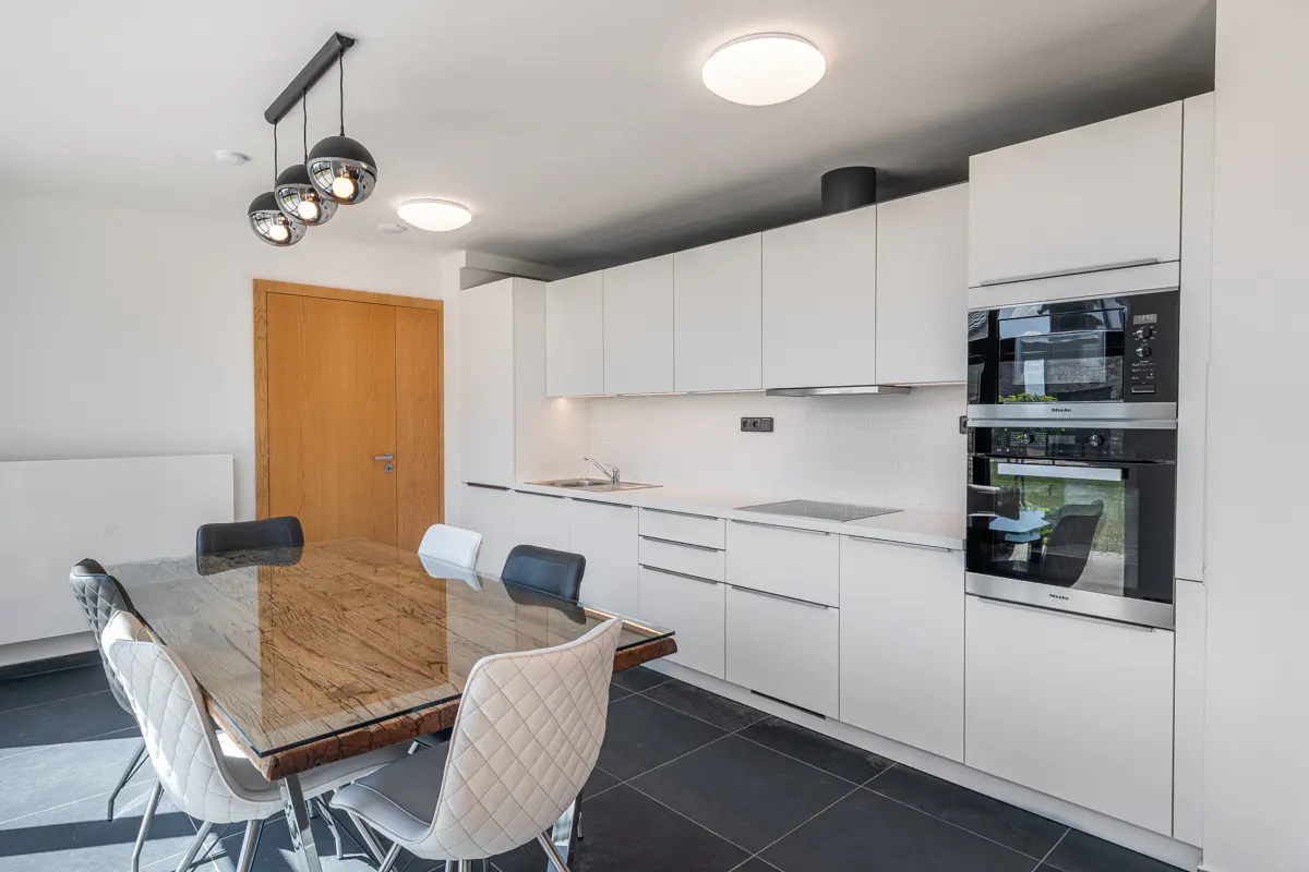 Bright kitchen with white cabinets, stainless steel appliances, and a wood table with gray chairs under a modern pendant light.