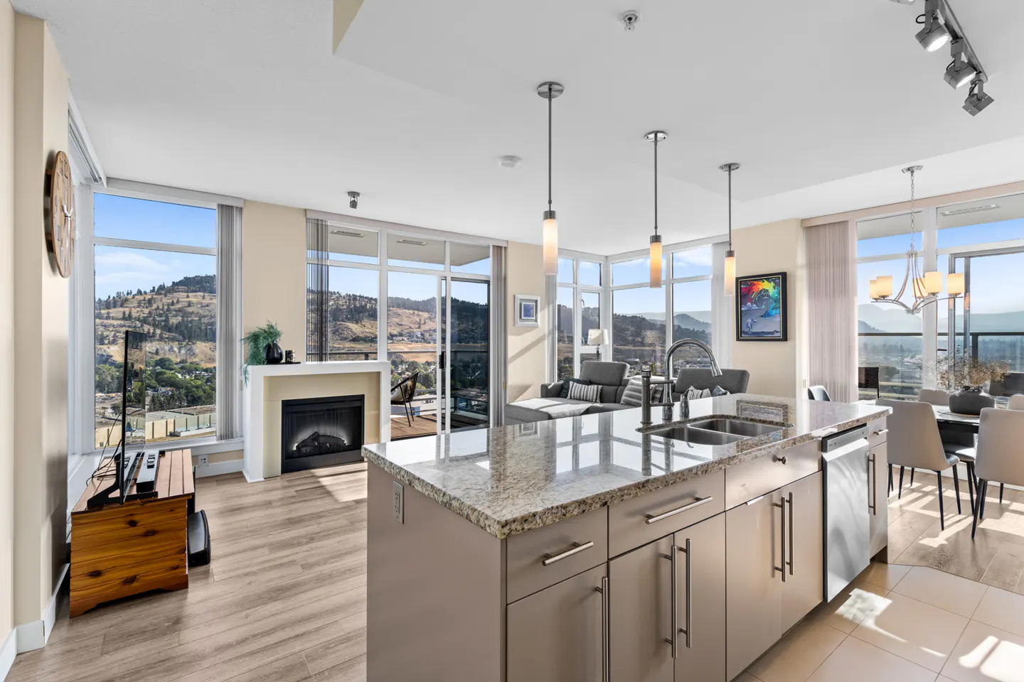 Modern open-concept kitchen with granite island, fireplace, and floor-to-ceiling windows overlooking a mountain landscape.
