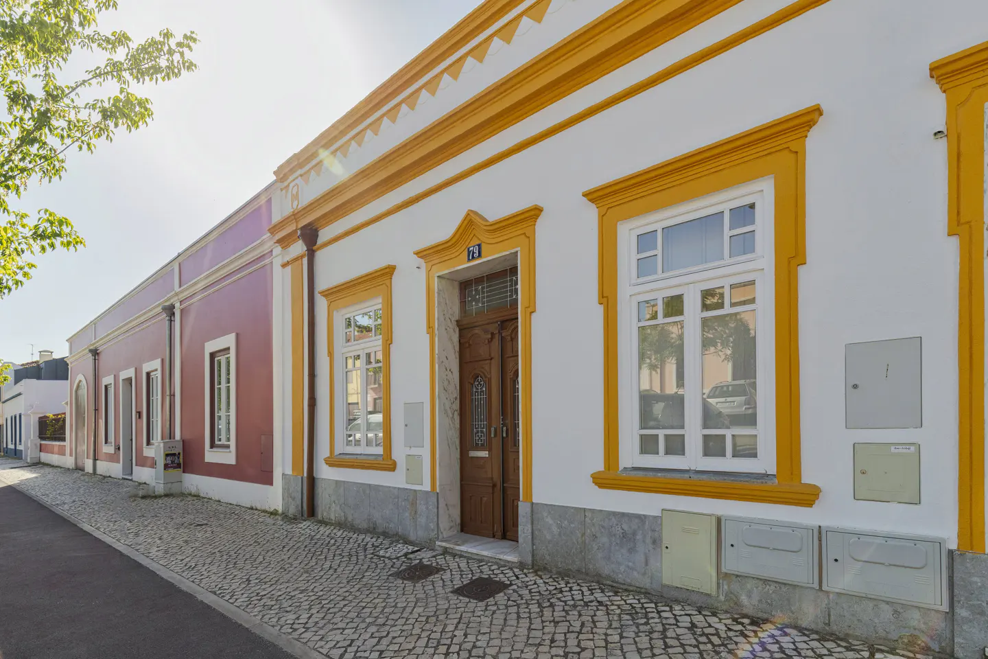 Exterior view of a white house with bright yellow trim, a wooden door, and white windows on a cobblestone street.