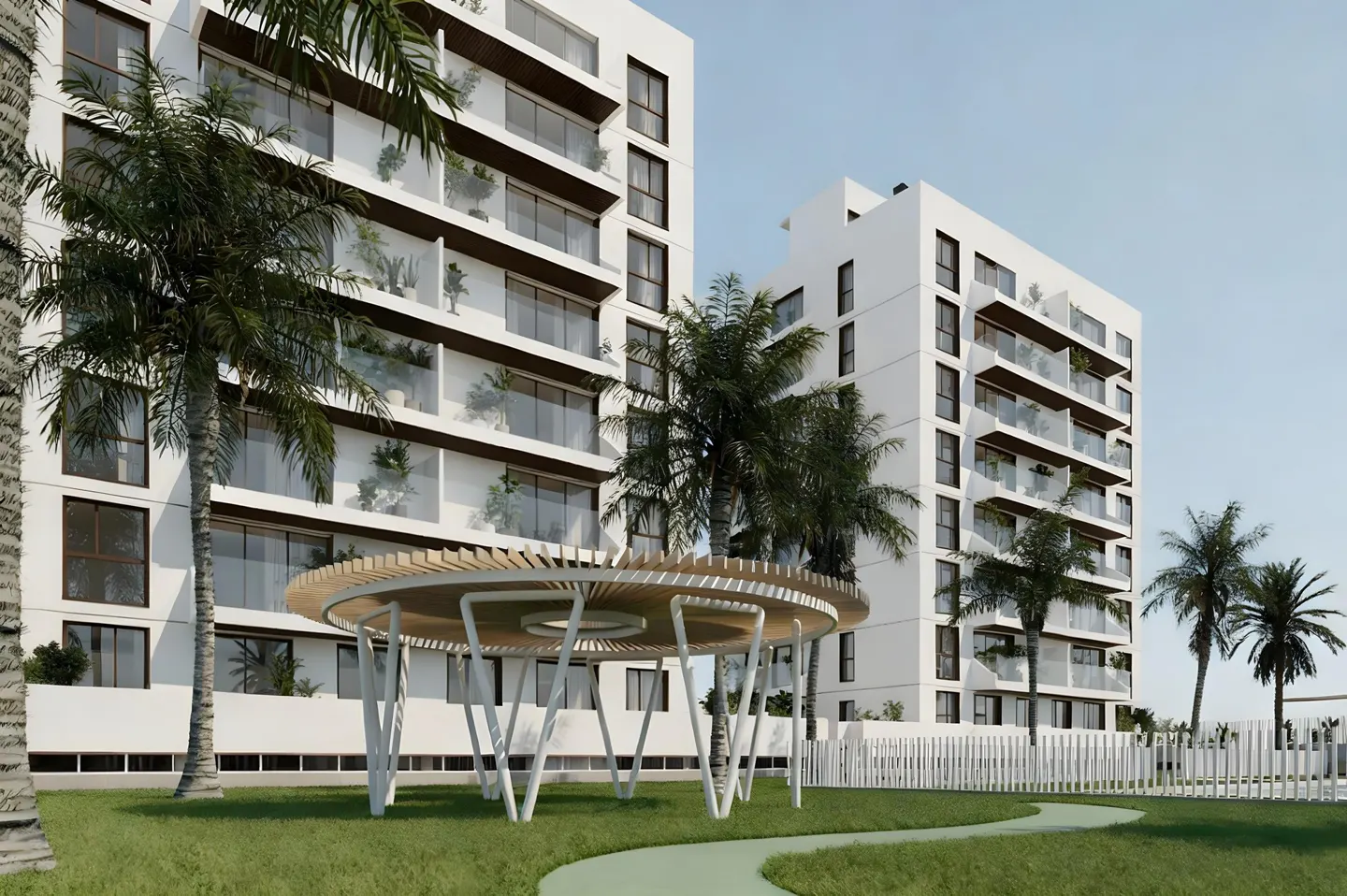 Modern white apartment buildings with balconies and palm trees. A circular gazebo sits on a green lawn.