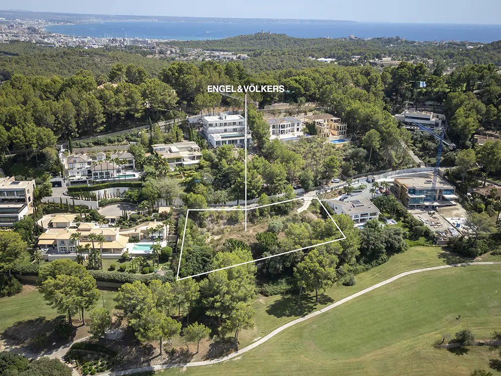 Aerial view of a vacant lot outlined in white, surrounded by green trees and luxury homes. Engel & Völkers logo visible.