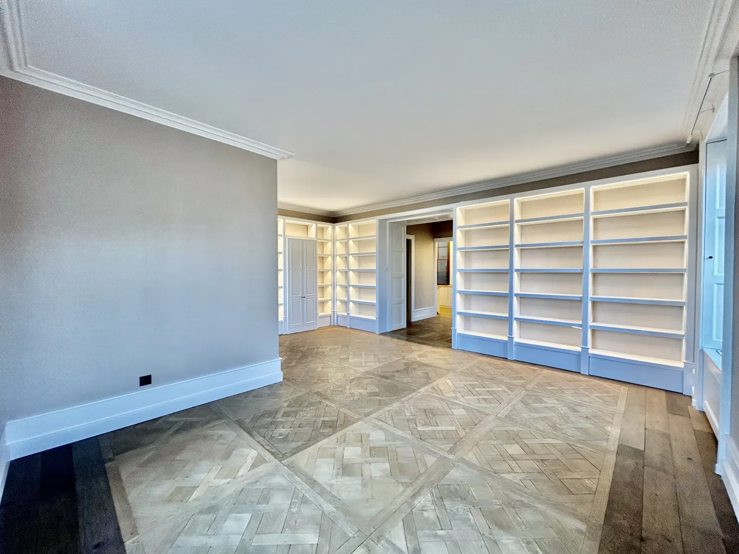 An empty room with parquet floors and built-in white bookshelves with lights.