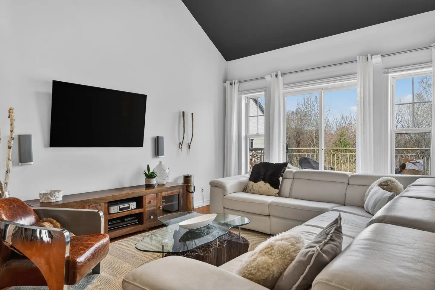 Bright living room with a black ceiling, white walls, and a large window. A white sectional sofa and a brown leather chair are in the room.