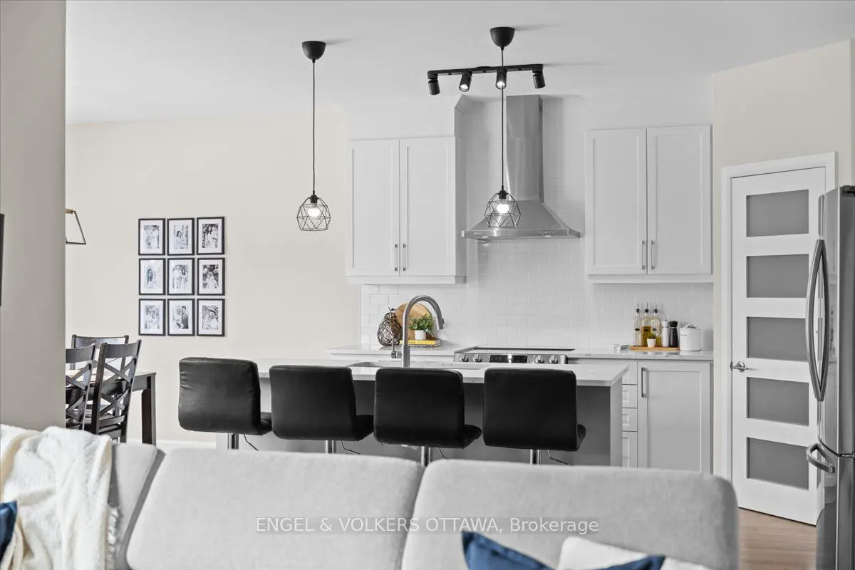 A bright, modern kitchen with white cabinets, black bar stools, and pendant lighting.