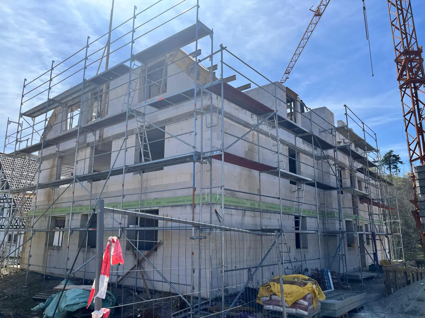A three-story building under construction is surrounded by scaffolding and a crane against a blue sky.