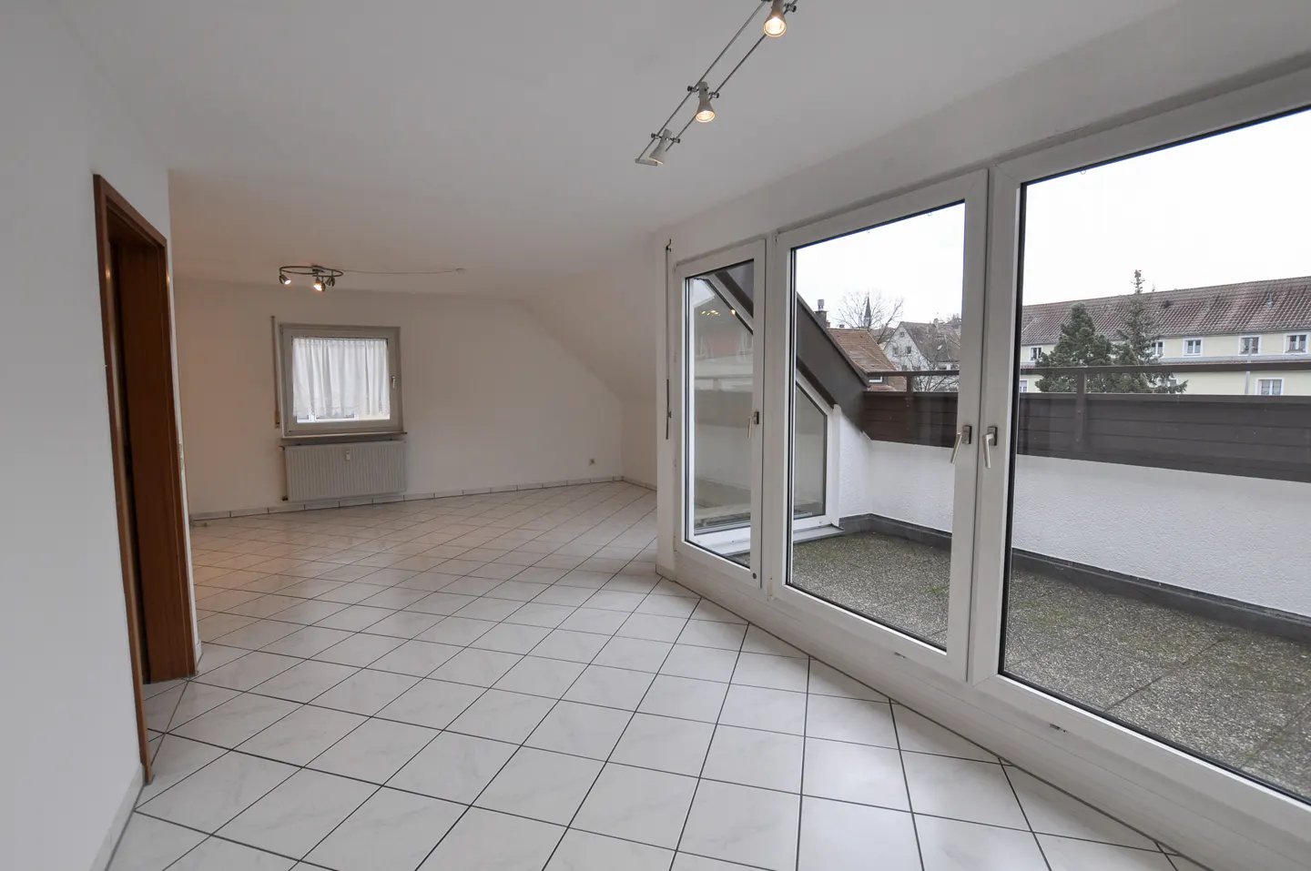 Bright, empty room with white tile floor and large windows to a balcony. A window and door are on the left wall.