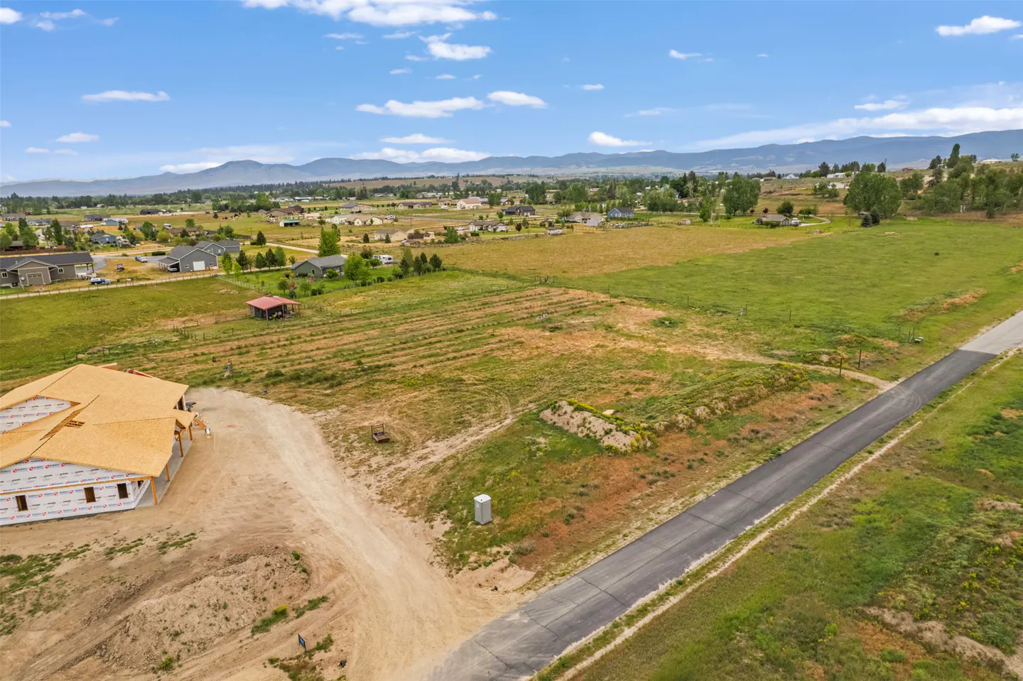 Aerial view of a new home under construction on a large lot with mountain views. Blue sky with scattered clouds.